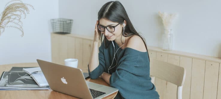bild von einer frau die mit kopfhörern vor einem laptop sitzt grin |