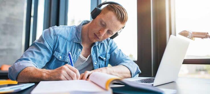 Bild von einem jungen Mann, der mit Laptop und Büchern an einem Schreibtisch sitzt