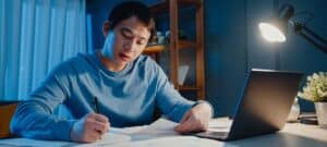 Bild eines jungen Mannes abends vor dem Laptop mit angeschalteter Schreibtischlampe
