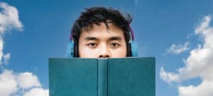 Junger Mann mit Over-Ear-Kopfhörern hinter einem aufgeschlagenen Buch
