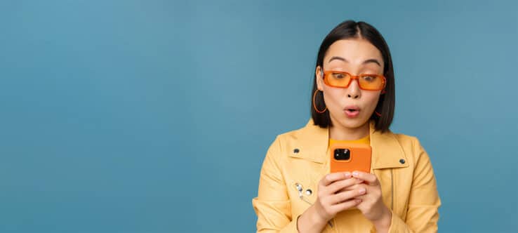 Bild von einer Frau mit gelber Jacke, die überrascht auf ihr Smartphone sieht