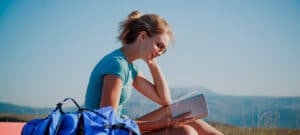 Bild von einer jungen Frau, die lesend in den Bergen sitzt