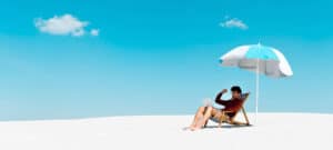 Foto von einem Mann, der mit Laptop unter einem Sonnenschirm am Strand sitzt